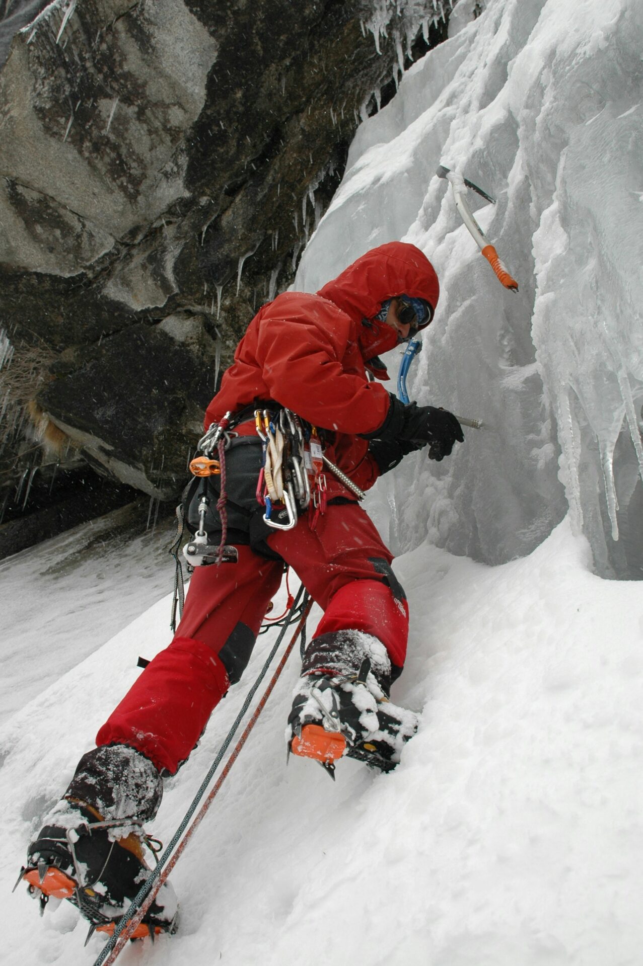 Un grimpeur équipé de matériel d'escalade, crampons et piolets, escalade une impressionnante cascade de glace gelée, entouré d'un paysage hivernal spectaculaire.